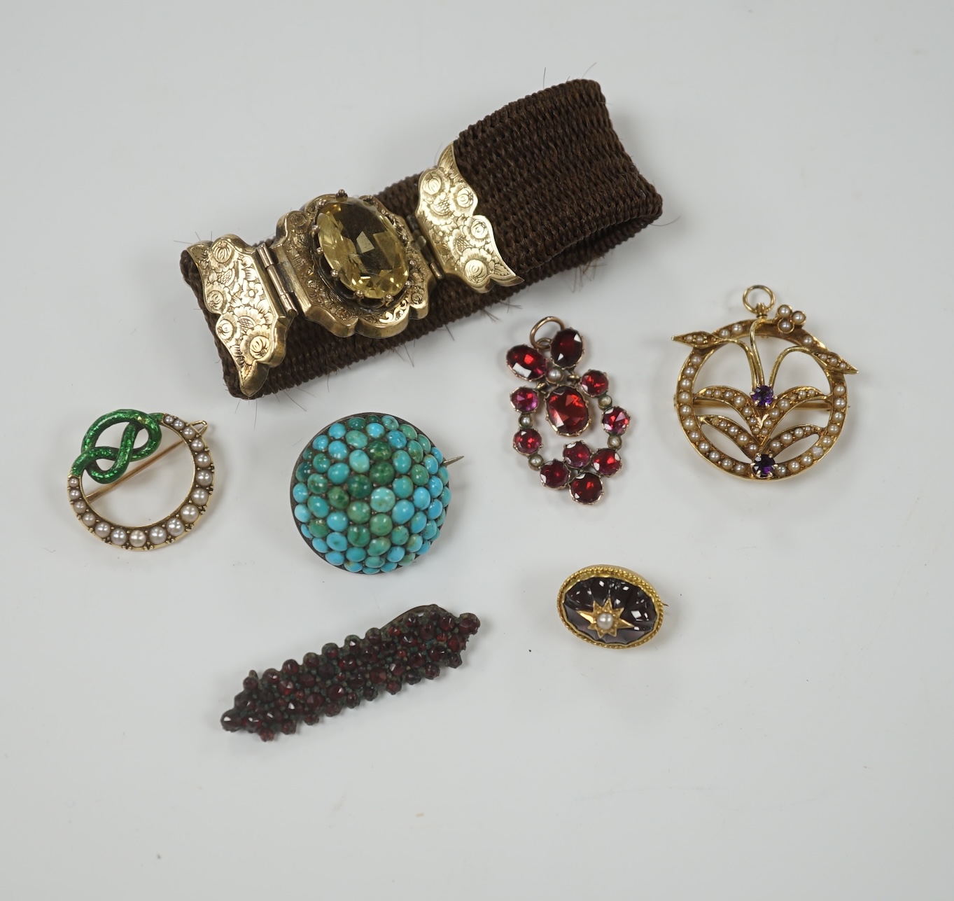 A Victorian yellow metal, garnet and split pearl cluster set drop pendant, 27mm, together with an enamelled and split pearl set knot brooch and five other items including a 14k, amethyst and seed peal set pendant brooch.